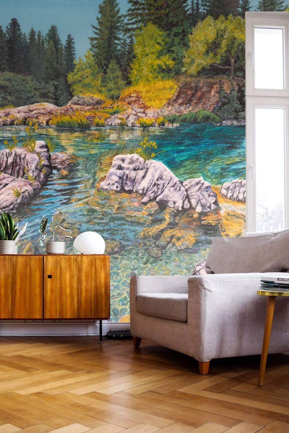 Sunlit Riverbank Mural by Jennifer Patten in a styled reading room with a pale armchair and warm wood cabinet