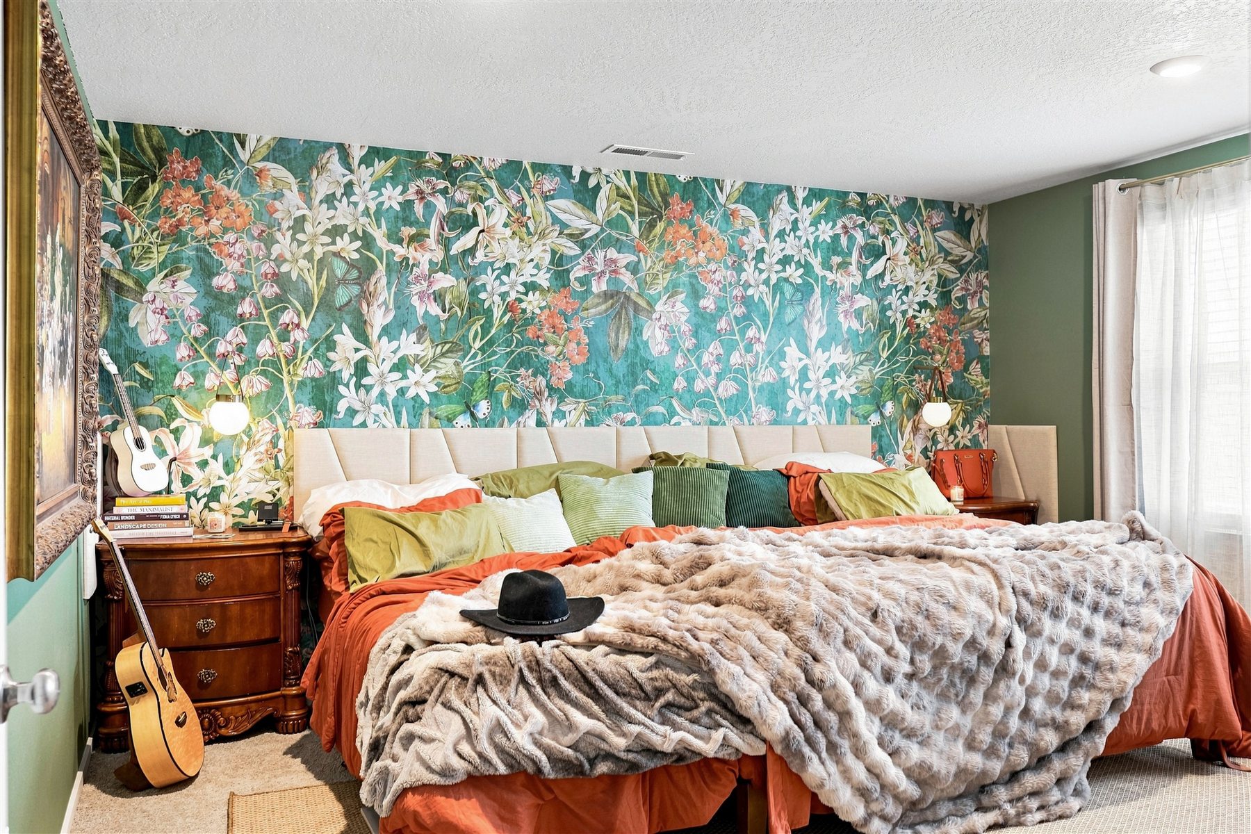 Teal botanical wallpaper behind a bed with rust bedding and green pillows in a finished Press Esc bedroom project.